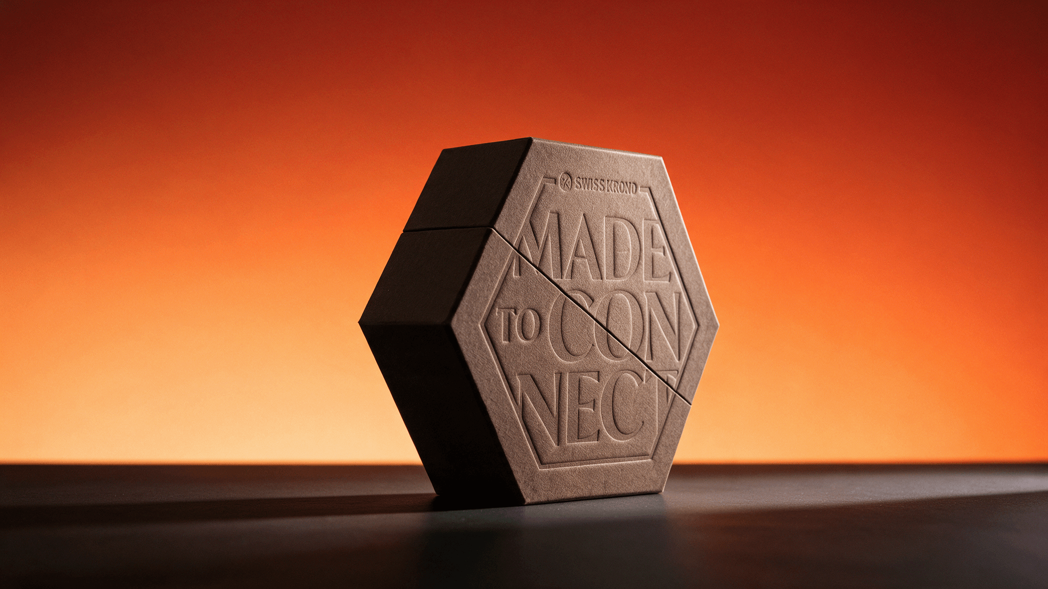 Die sechseckige Box „Made to Connect“ mit geprägtem Schriftzug vor orangem Hintergrund.
