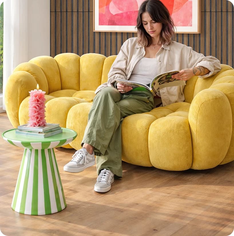 Junge Frau liest auf einem gelben Sofa, daneben ein grün-weiß gestreifter Beistelltisch auf dem kiwi now Boden