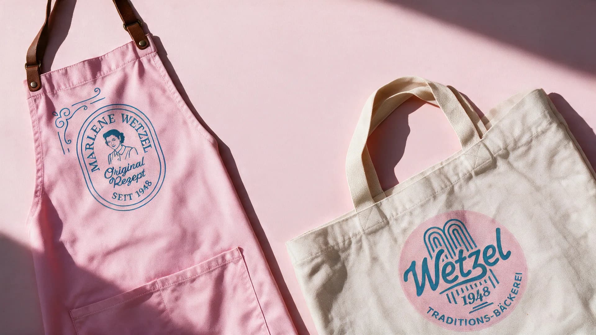 Eine rosa Schürze mit „Marlene Wetzel Original Rezept“ und eine Stofftasche mit dem neuen Wetzel-Siegel auf Rosa