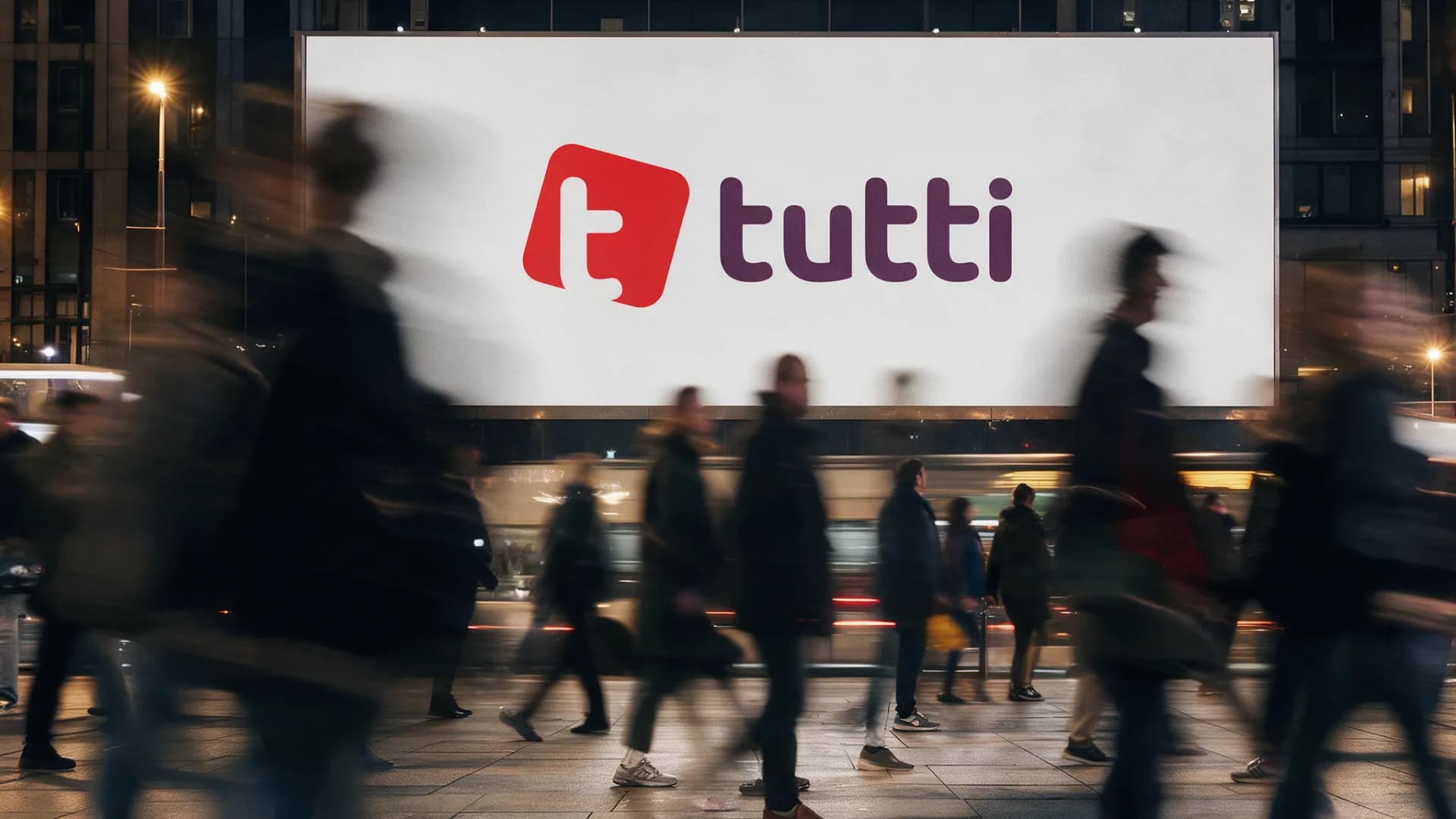 A large poster with the tutti logo in the evening, passers-by in motion in front of it